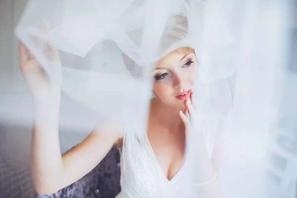 Beautiful young bride with wedding makeup and hairstyle in bedroom.Beautiful bride portrait with veil over her face. Closeup portrait of young gorgeous bride. Wedding.