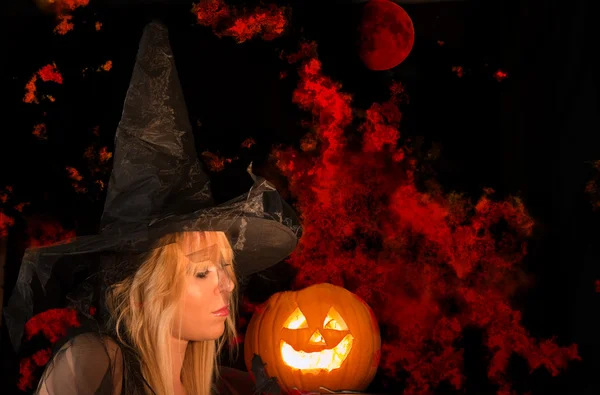 Halloween witch with a pumpkin and a scary burning sky background