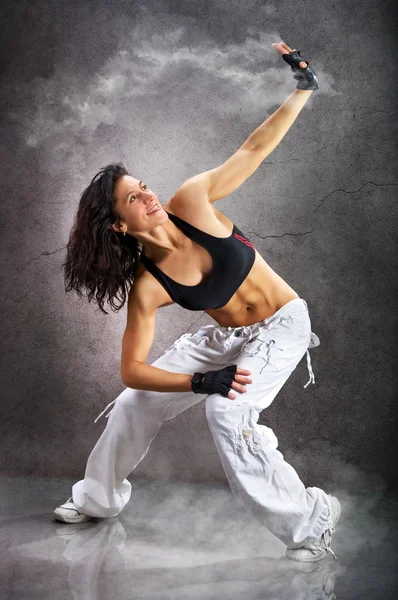 Young beautiful athletic woman dancing modern dance hip-hop on wall background with smoke smoke