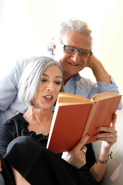 Aged couple reading a book on the couch