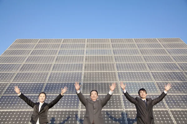 Businesspeople with Arms Outstretched in front of Solar Panel