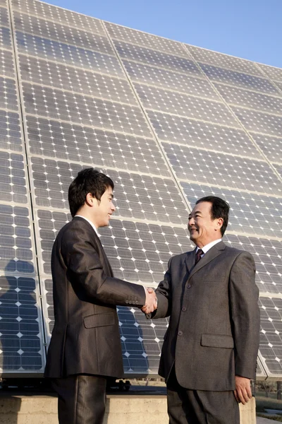 Shaking hands in front of solar panels