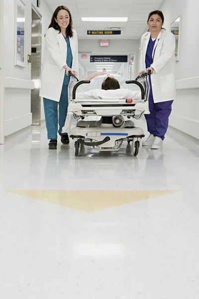 Doctors pushing patient in bed through corridor