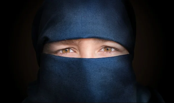 Eyes of young woman veiled with blue niqab scarf. Low key photo.