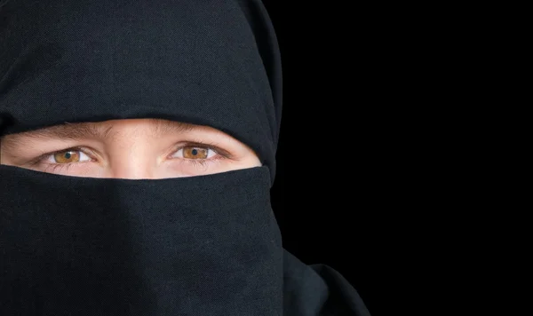 Eyes of young woman in black niqab scarf. Isolated on black background