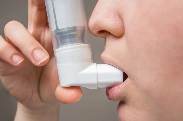 Face of woman suffering from asthma using inhaler.