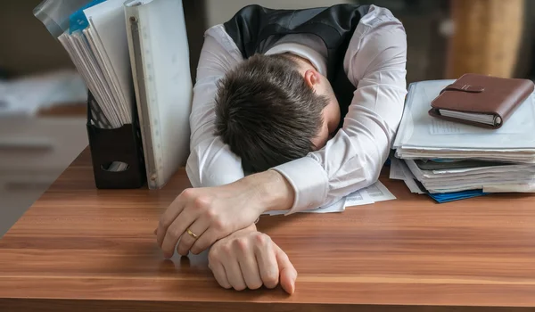 Tired workaholic is sleeping on desk in office.
