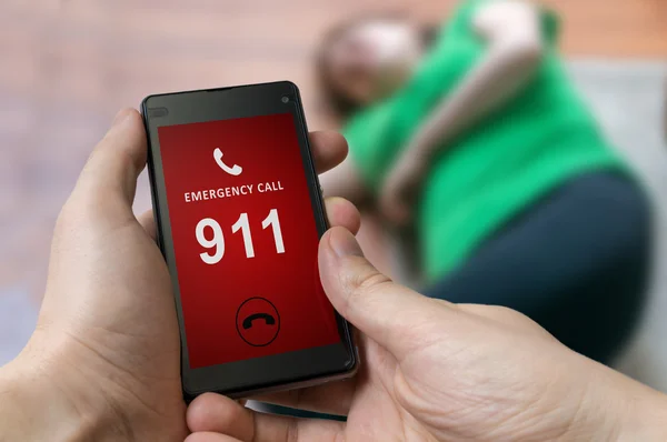 Man dialing emergency (911 number) on smartphone. Injured woman had accident and is lying on the floor.
