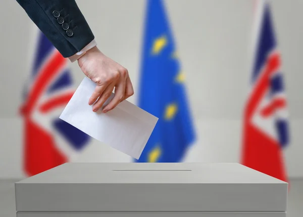 Election or referendum in Great Britain. Voter holds envelope  in hand above vote ballot.