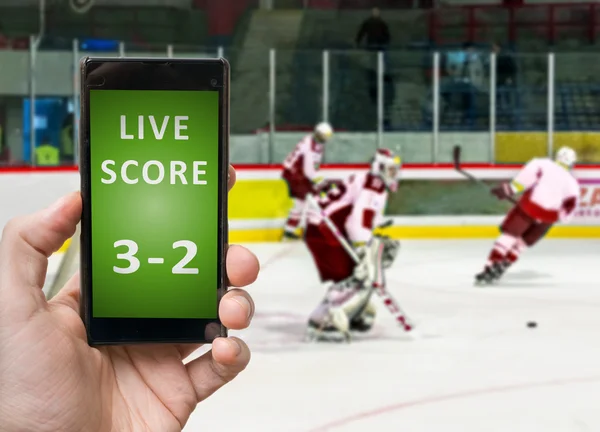 Man is watching ice hockey and holds smartphone in hand with live score.