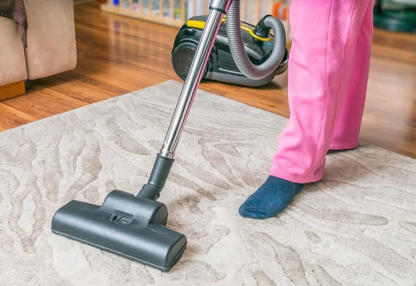 Woman is cleaning carpet with vacuum cleaner.