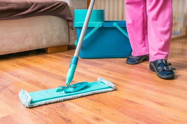 Woman is mopping wooden floor with mop.