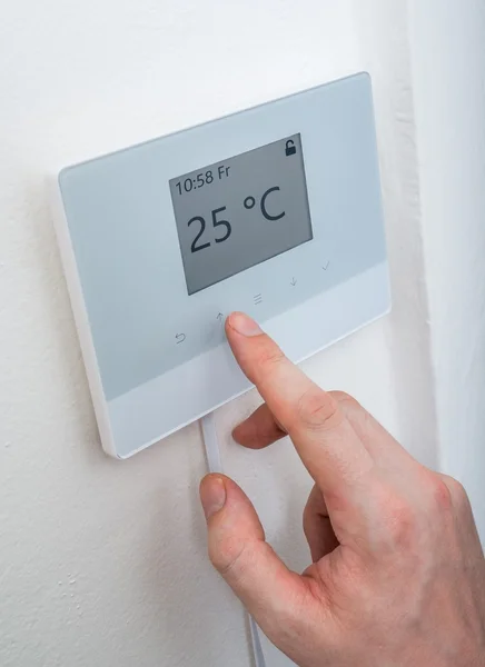 Heating concept. Man is adjusting temperature in room on electronic central thermostat control.