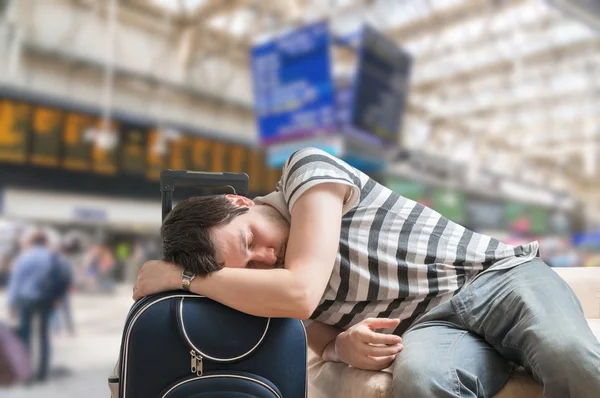 Delayed train concept. Tired and exhausted passenger is sleeping on baggage in train station.