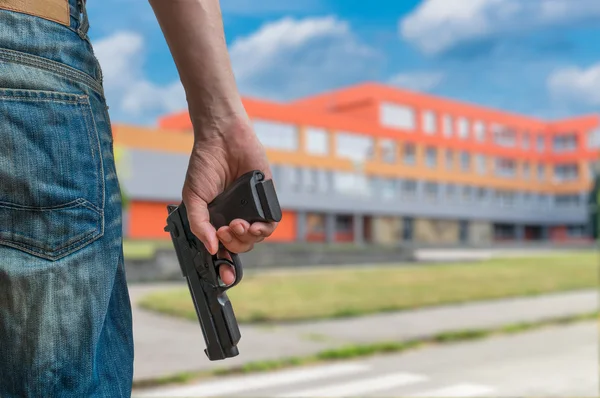 Gun control concept. Young armed man holds pistol in hand in public place near high school.
