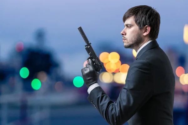 Secret agent or spy holds pistol in hand at dusk.