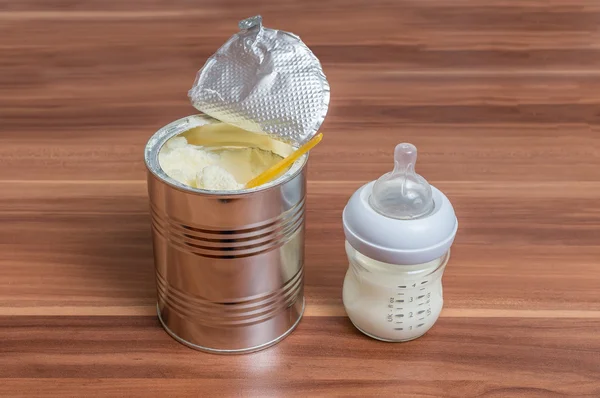 Powdered milk formula in can and bottle for feeding baby on wood