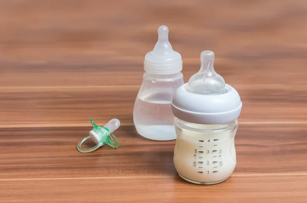 Bottles with milk for feeding baby on wooden background.