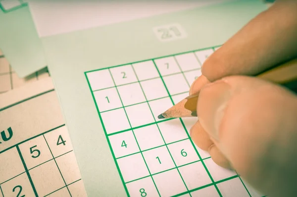 Hand is writing numbers in grid of popular logic game sudoku.