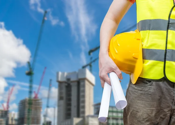 Building construction concept. Worker (engineer) with blueprint and cranes in background.