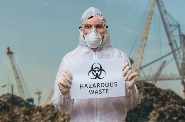 Technician in coverall in landfill warns against dangerous hazardous waste and hazmat.