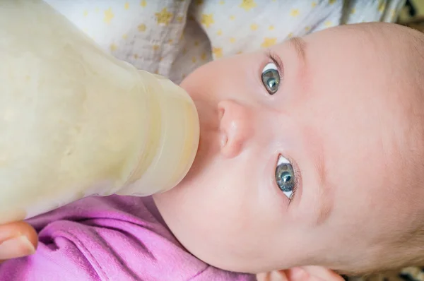 Feeding newborn concept. Little baby girl is drinking milk formula from bottle.