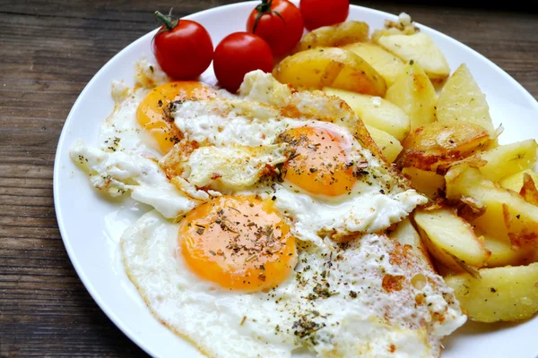 Big round plate full of fried eggs, french fries and cherry tomatoes - a traditional continental breakfast