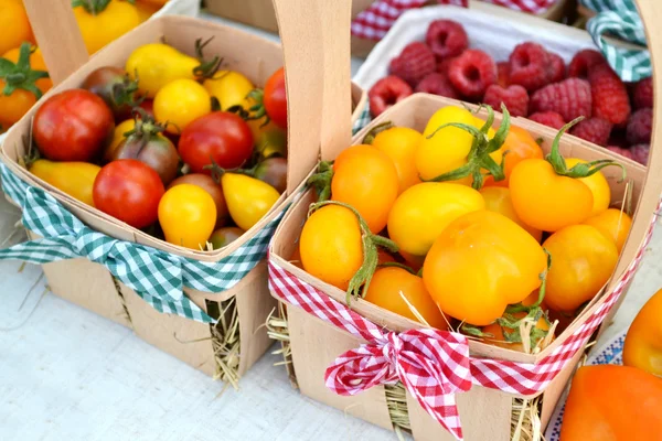 Small red, brown and yellow organic cherry tomatoes of different kinds in buckets on a street market