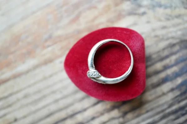 Red heart shaped ring box with platinum engagement ring on wooden table