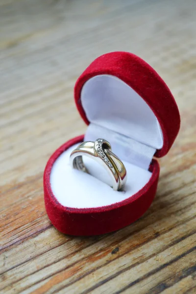 Red heart shaped ring box with platinum engagement ring on wooden table