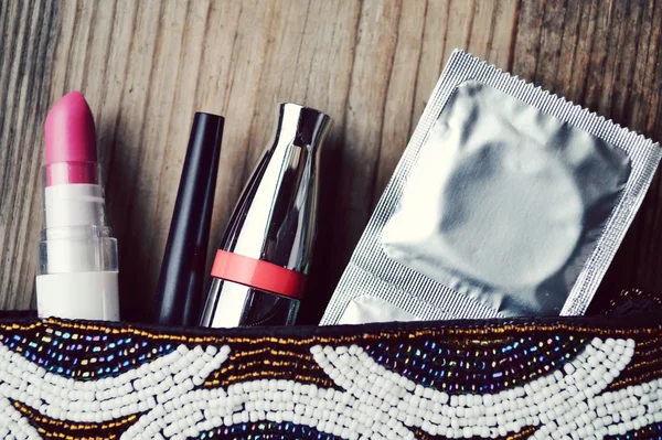 Couple of condoms and a cosmetics set with black mascara, pink and red nail polish and lipstick and eyelash curler isolated on white