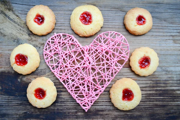 Romantic concept with handmade pink heart and lots of homemade cookies with jam on wooden table