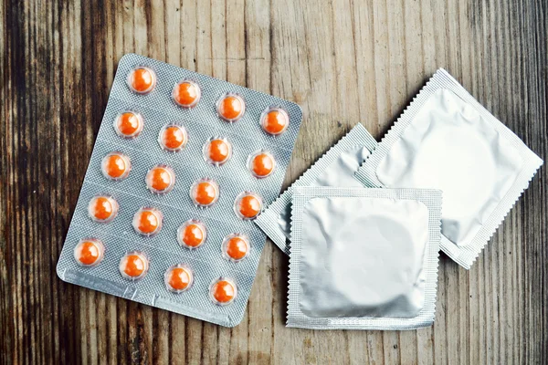 Three condoms and orange birth control pills on wooden table