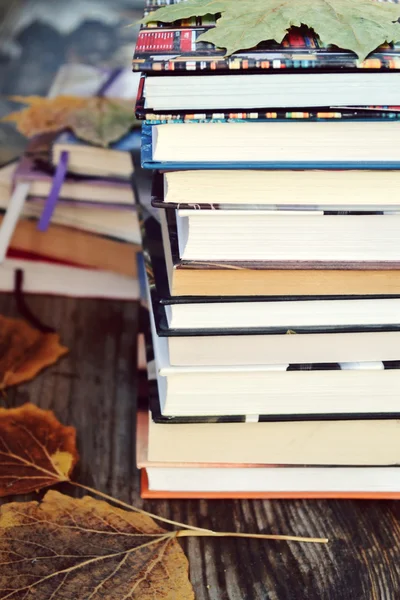 Pile of books with autumn leaves on wooden desk