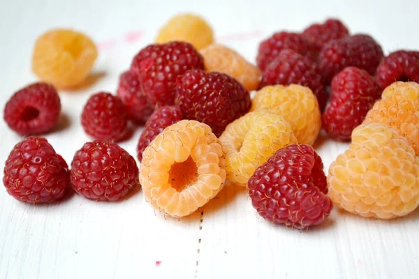Bright pink and yellow raspberries on white wooden board