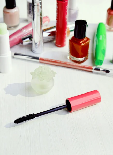 Pink mascara stick, eyeliner, lipstick, pencil and other cosmetics on the white dressing table