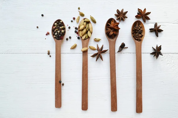 Four spoons full of different spices - cardamom, anise stars and peppers