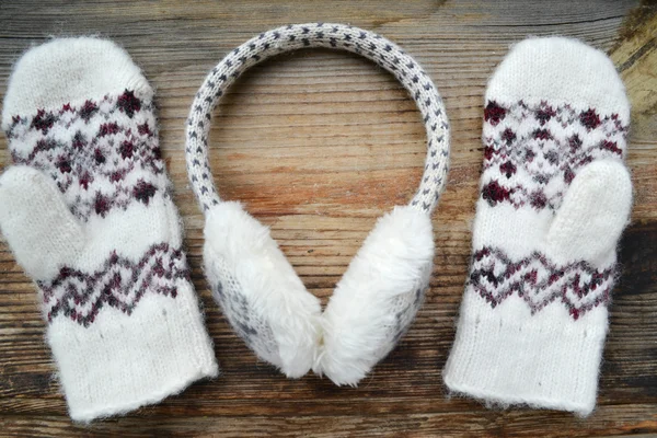 Soft woolen mittens with winter headphones on wooden table