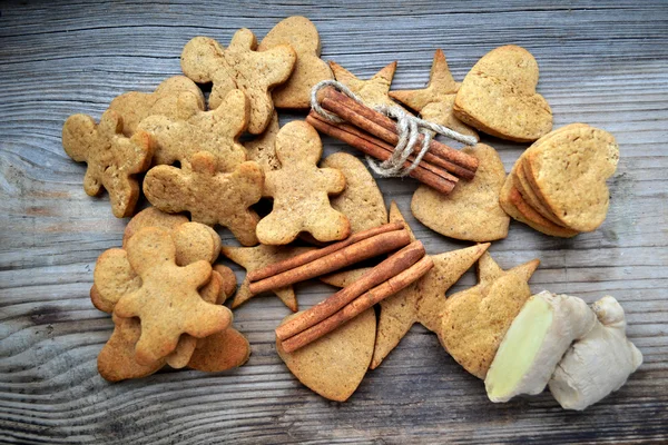 Gingerbread cookies in shapes of heart, star and man with cinnamon stick and ginger root on wooden table