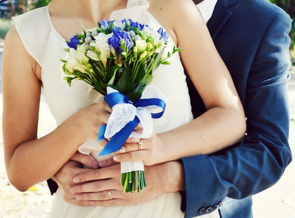 Groom hugging his beautiful bride who is holding a wedding bouquet of apricot and blue roses