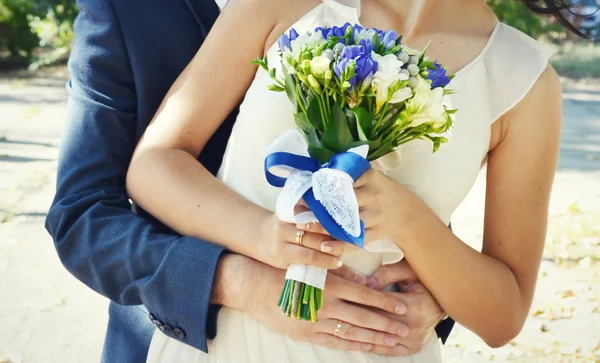 Groom hugging his beautiful bride who is holding a wedding bouquet of apricot and blue roses