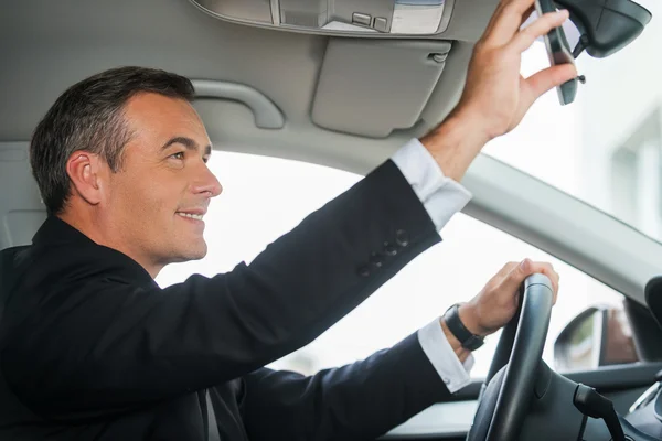 Mature man in formalwear adjusting mirror in car