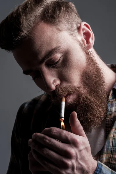 Young bearded man lighting up a cigarette