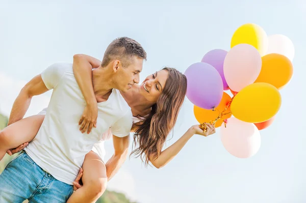 Young man carrying  girl with colorful balloons