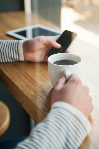 Man holding smartphone while enjoying coffee in cafe