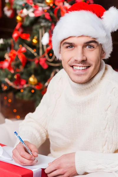 Man in Santa hat writing Christmas letter