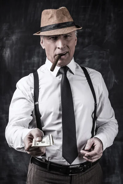 Senior man in hat and suspenders stretching out money