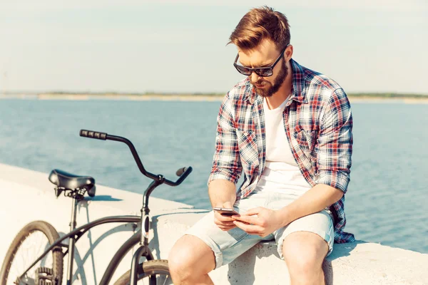 Man holding mobile phone near his bicycle