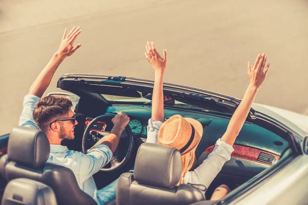Couple keeping arms raised  in convertible