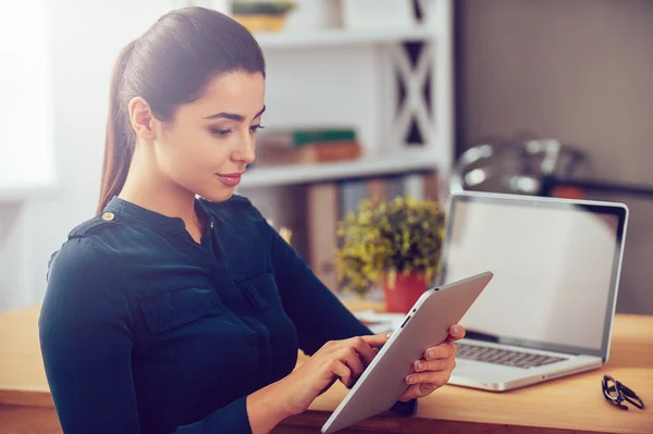 Woman working on digital tablet while sitting at her working place in office